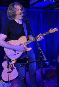 Tom Campbell playing guitar and singing into a microphone