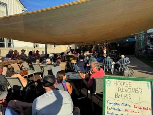 a group of people sitting at tables under a tent listening to live music at house divided brewery
